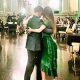 Couple dancing closely in a sunlit room with onlookers.