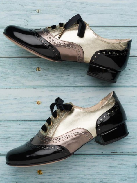 Pair of black and beige women's dress shoes on wooden floor.