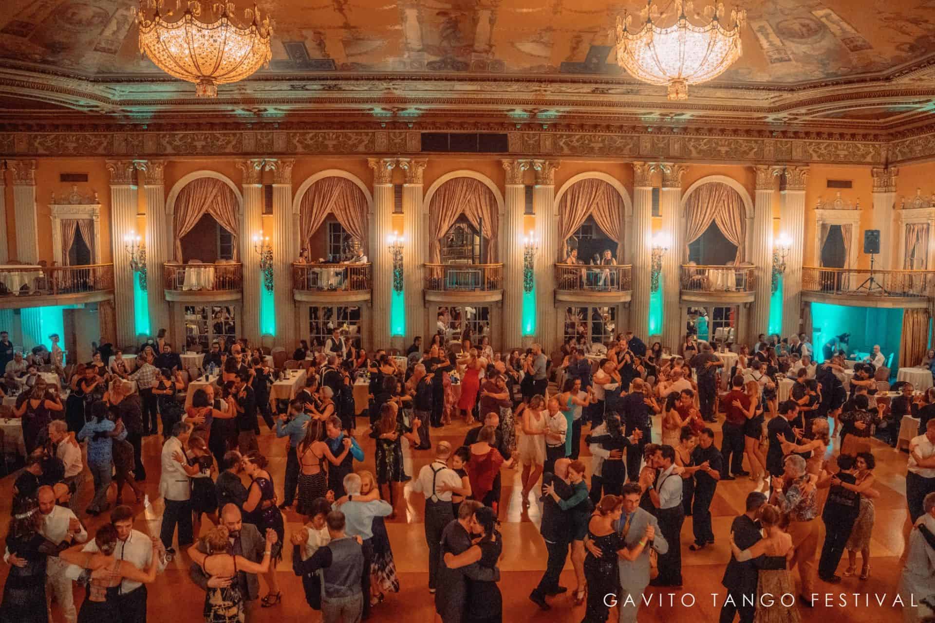 A grand ballroom filled with people dancing in elegant attire.