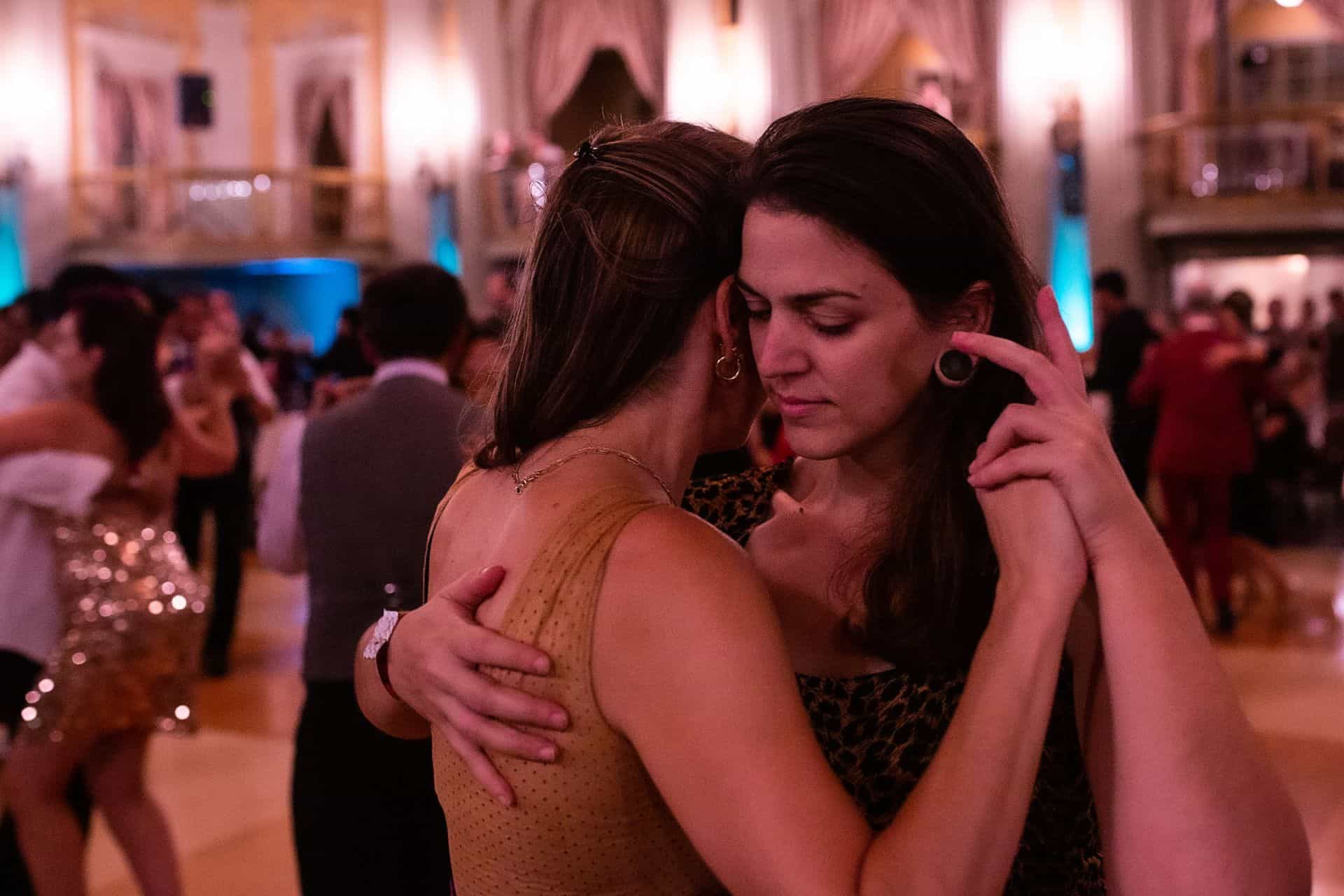 Two women warmly embracing in a dimly lit room.