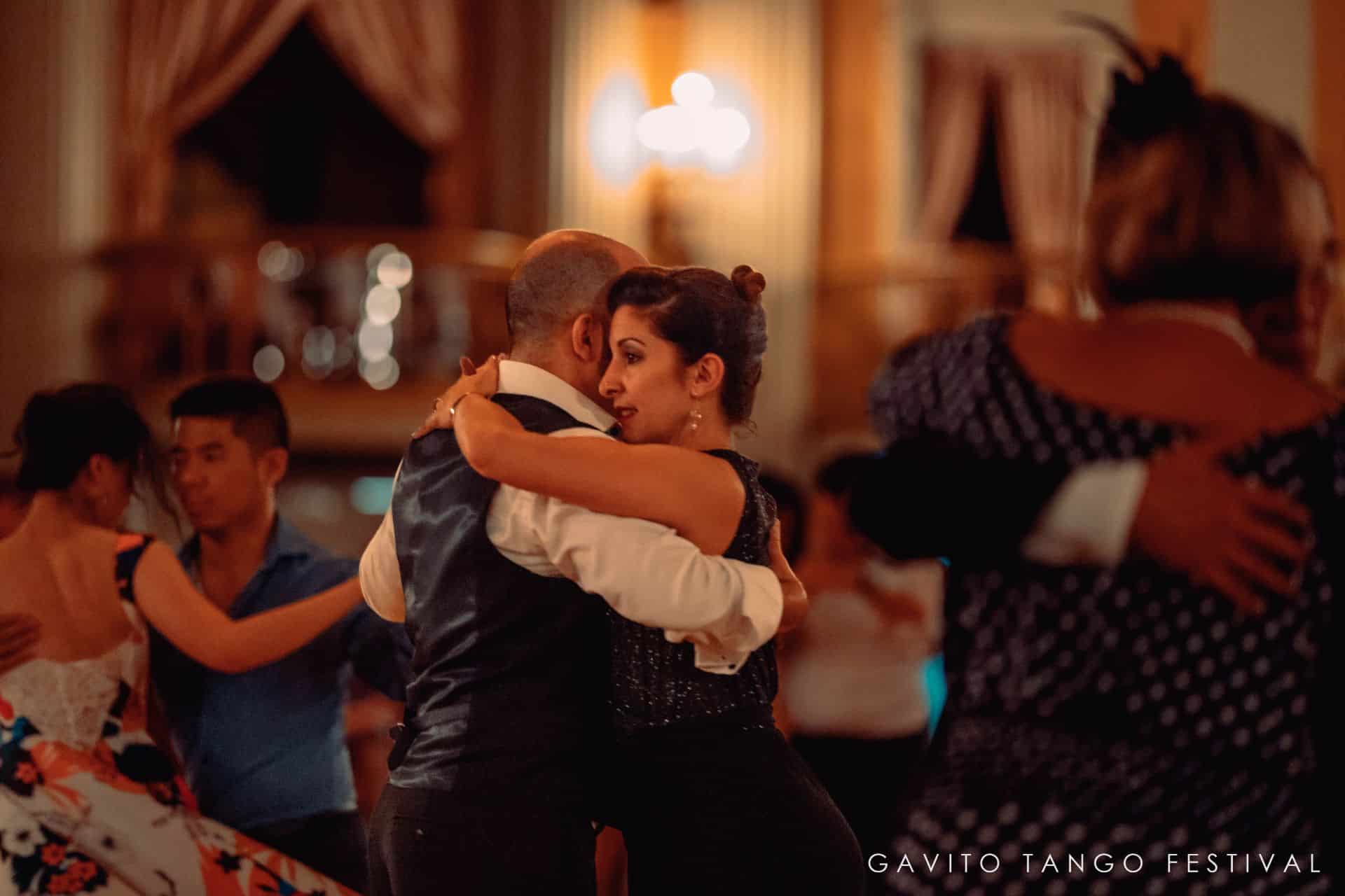 A couple dances closely in a warmly lit ballroom.