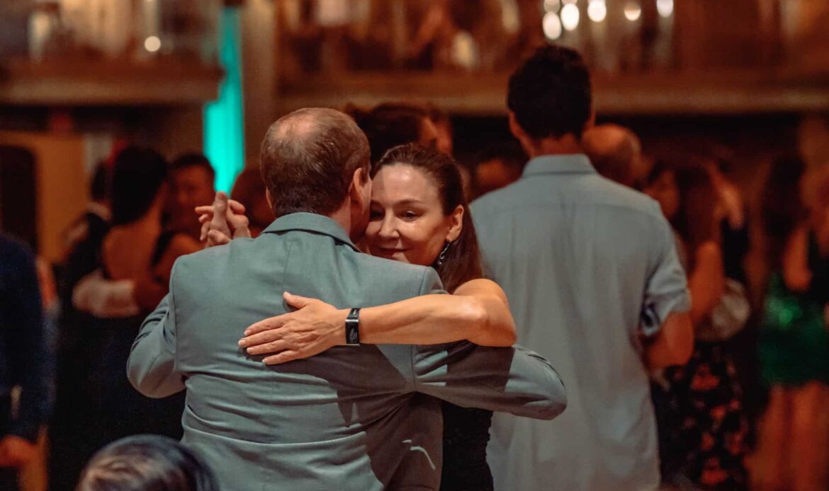 Two people warmly embracing in a crowded indoor setting.