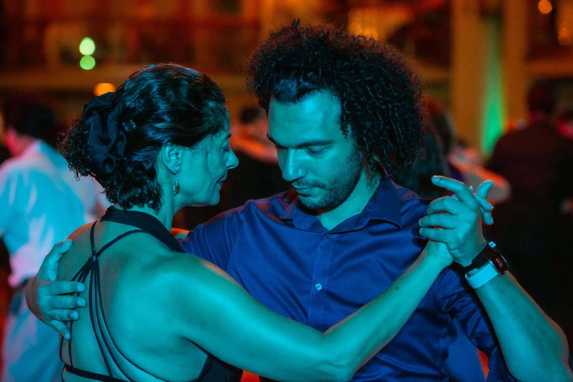 A couple dancing closely in dim blue and orange lighting.