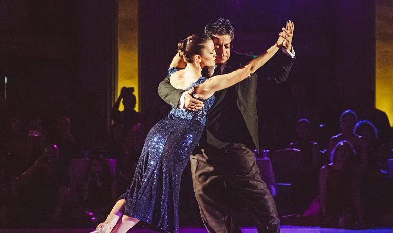 A couple dances passionately on a stage under purple lights.