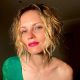 Woman with blonde curly hair and red lipstick in green top.