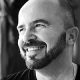 Smiling bald man with a beard in black and white portrait.