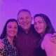 Three friends smiling together under purple lighting.