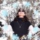 Person wearing sunglasses with a snowy tree background.