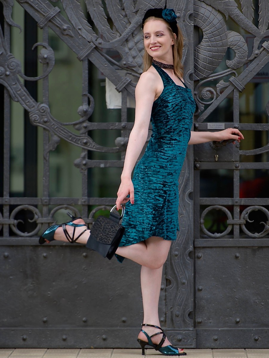 Woman in a teal dress stands on a city street near a metal fence.