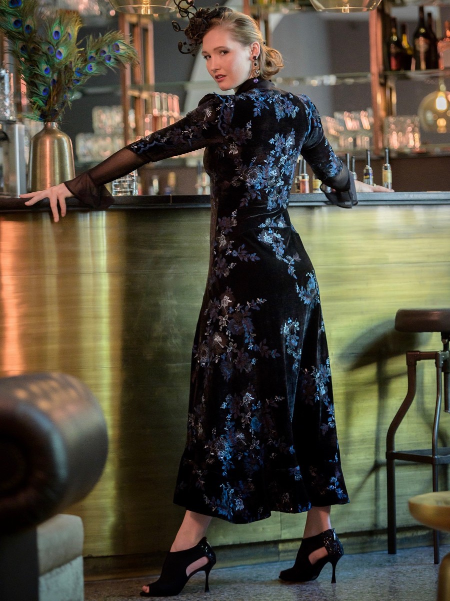 Person in a dark floral dress standing near water at night.