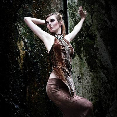 A woman posing confidently in a sheer dress against a dark, textured background.