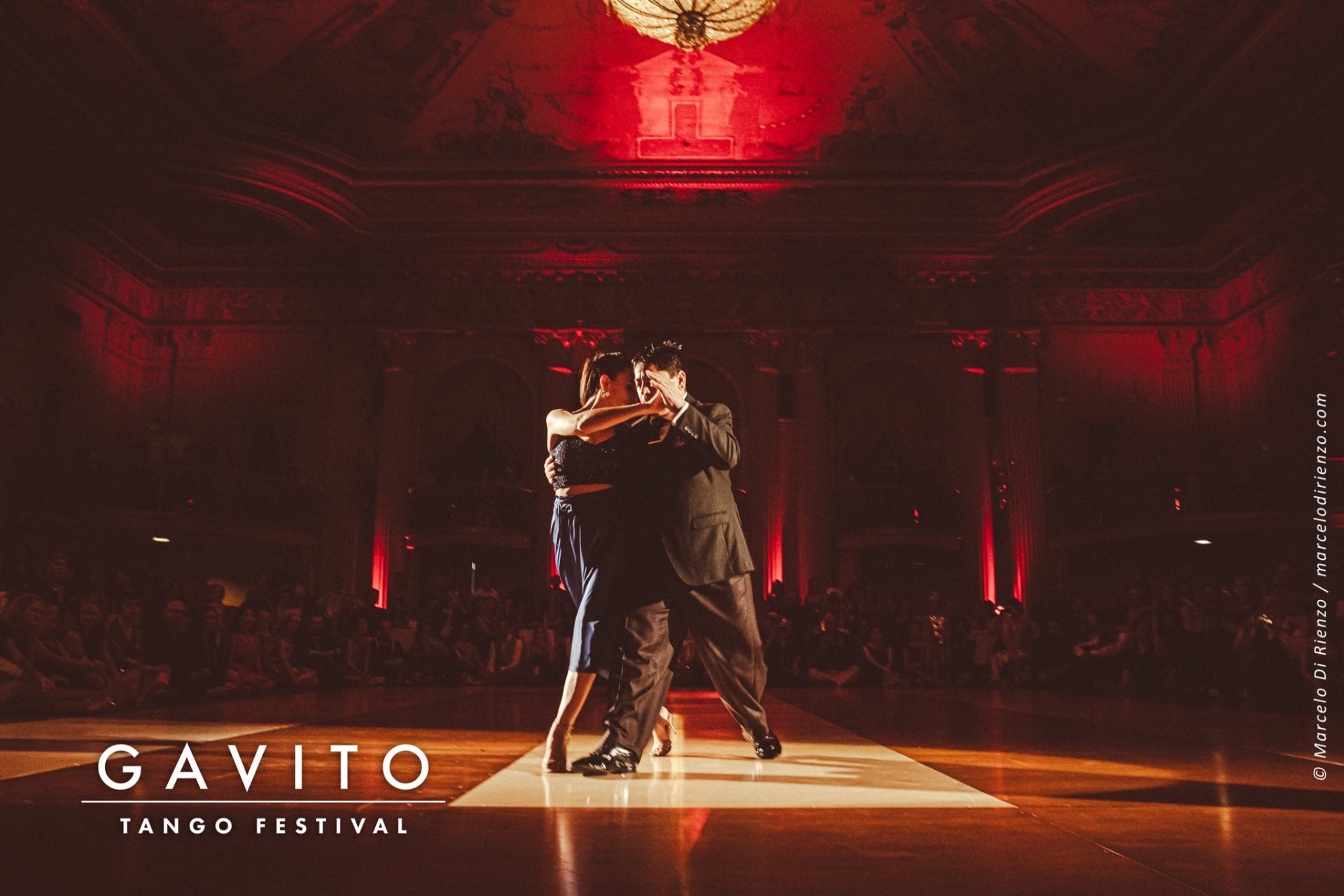 Couple dancing the tango on a dimly lit stage with red lighting.