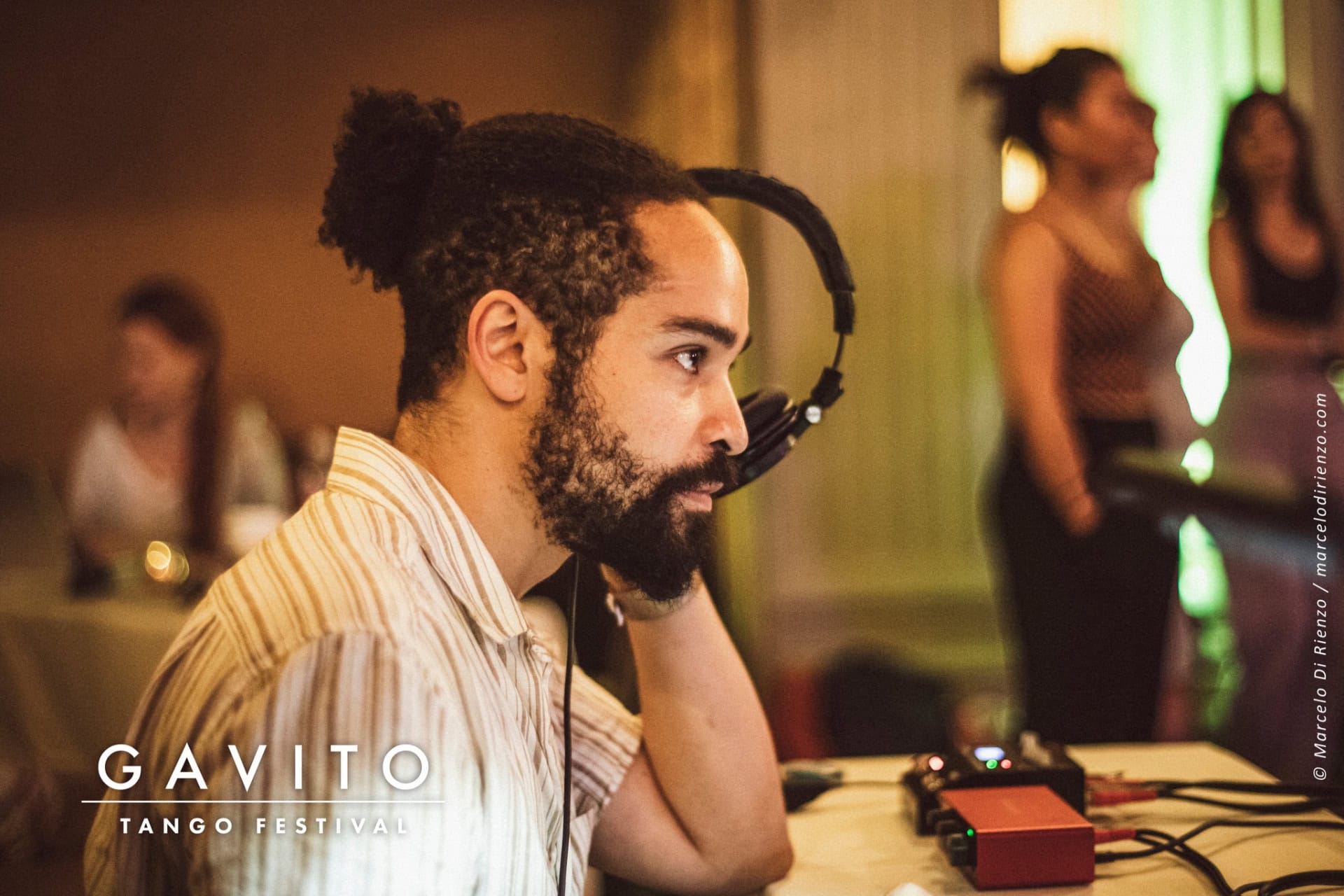 Man with a beard and bun sitting thoughtfully indoors.