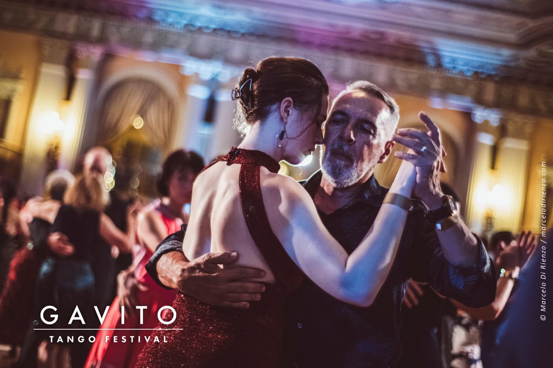 Couple dancing closely at a lively party with vibrant lighting.