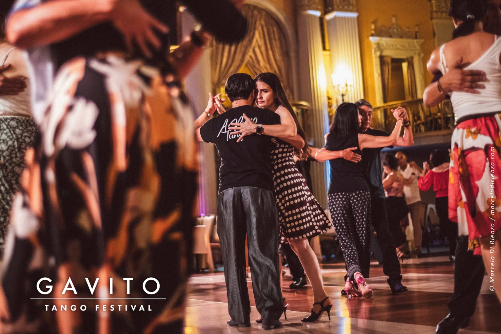 Couple dancing closely in a warmly lit room with onlookers.