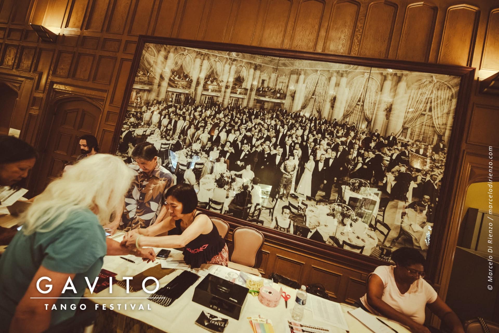 A man paints a large mural with a crowd scene in a studio.