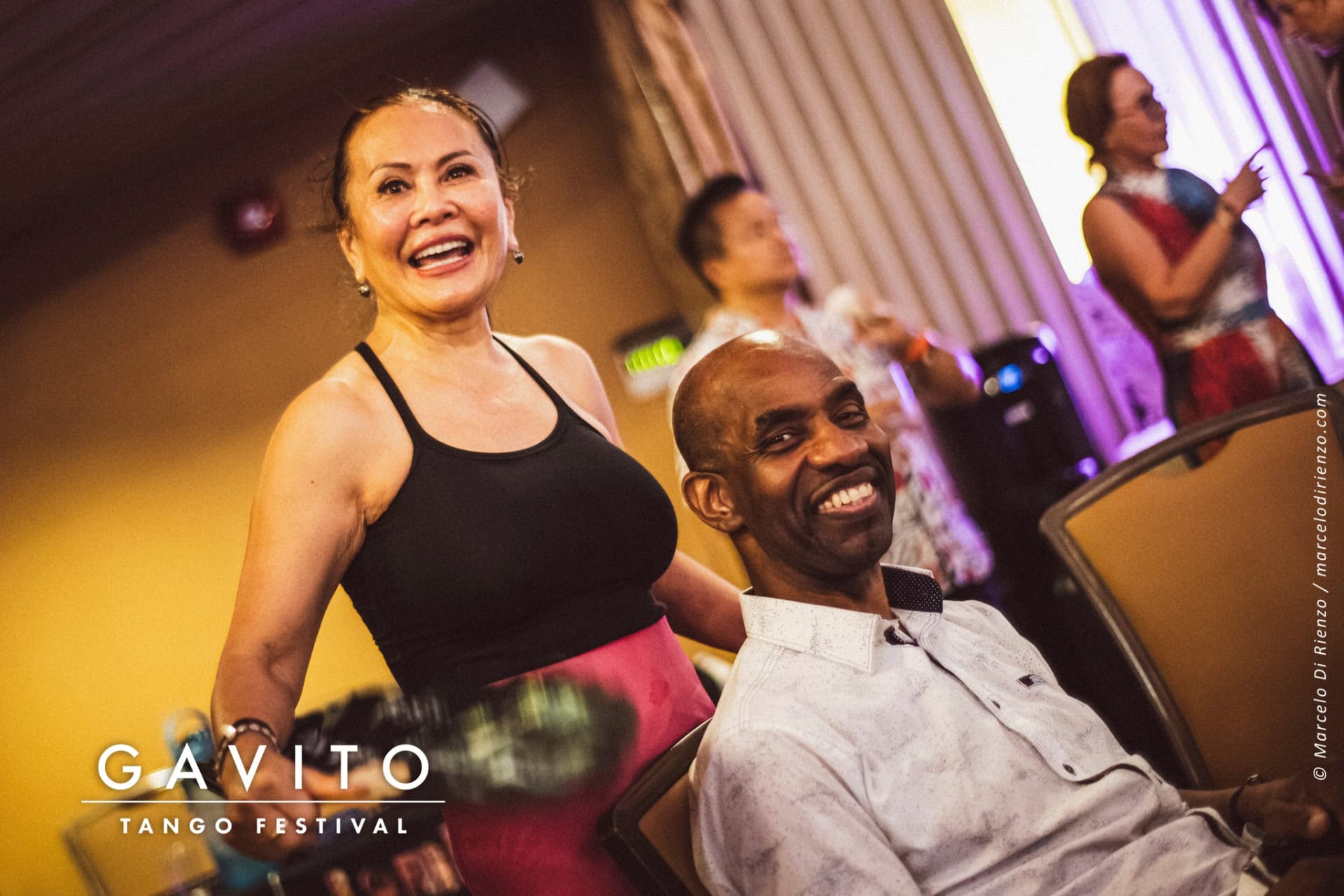 Smiling woman and seated man in a lively indoor setting.