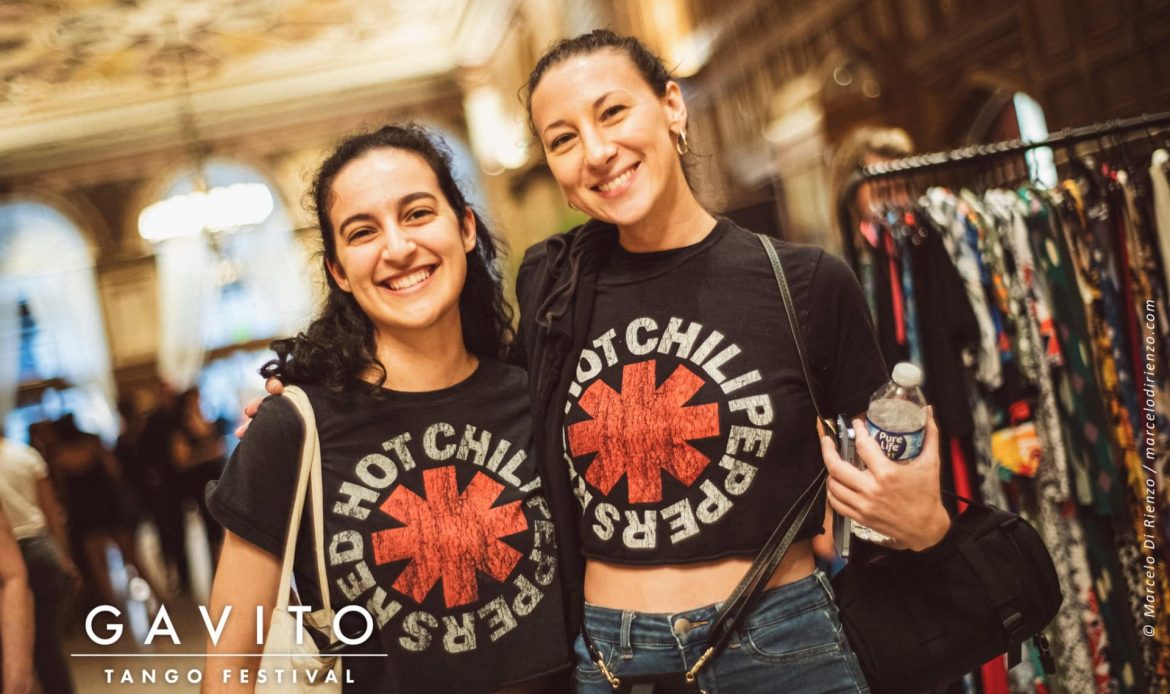 Two women smiling, wearing matching Red Hot Chili Peppers shirts at a lively event.