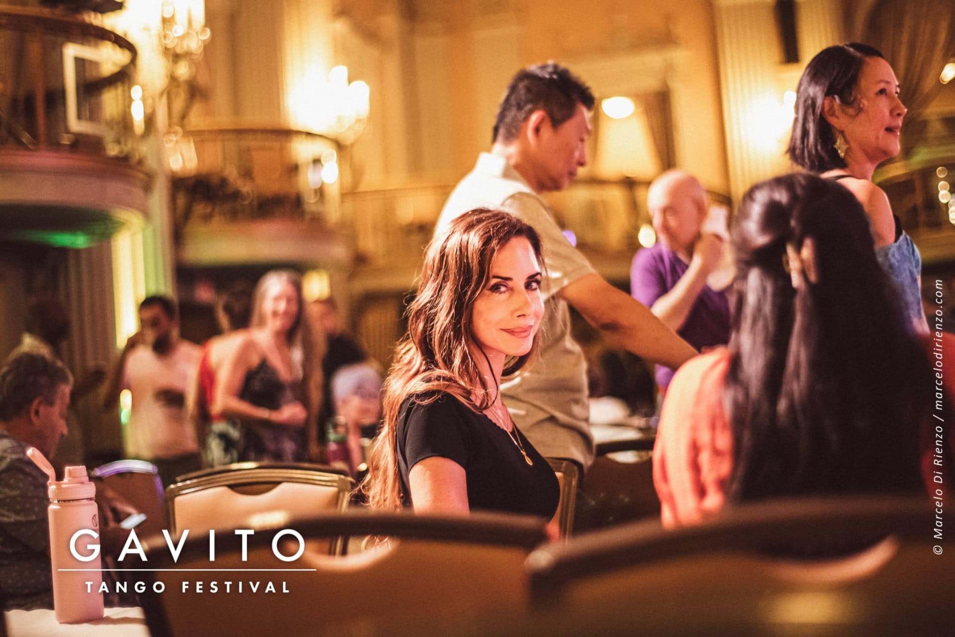 A woman sitting alone in a crowded, lively bar.