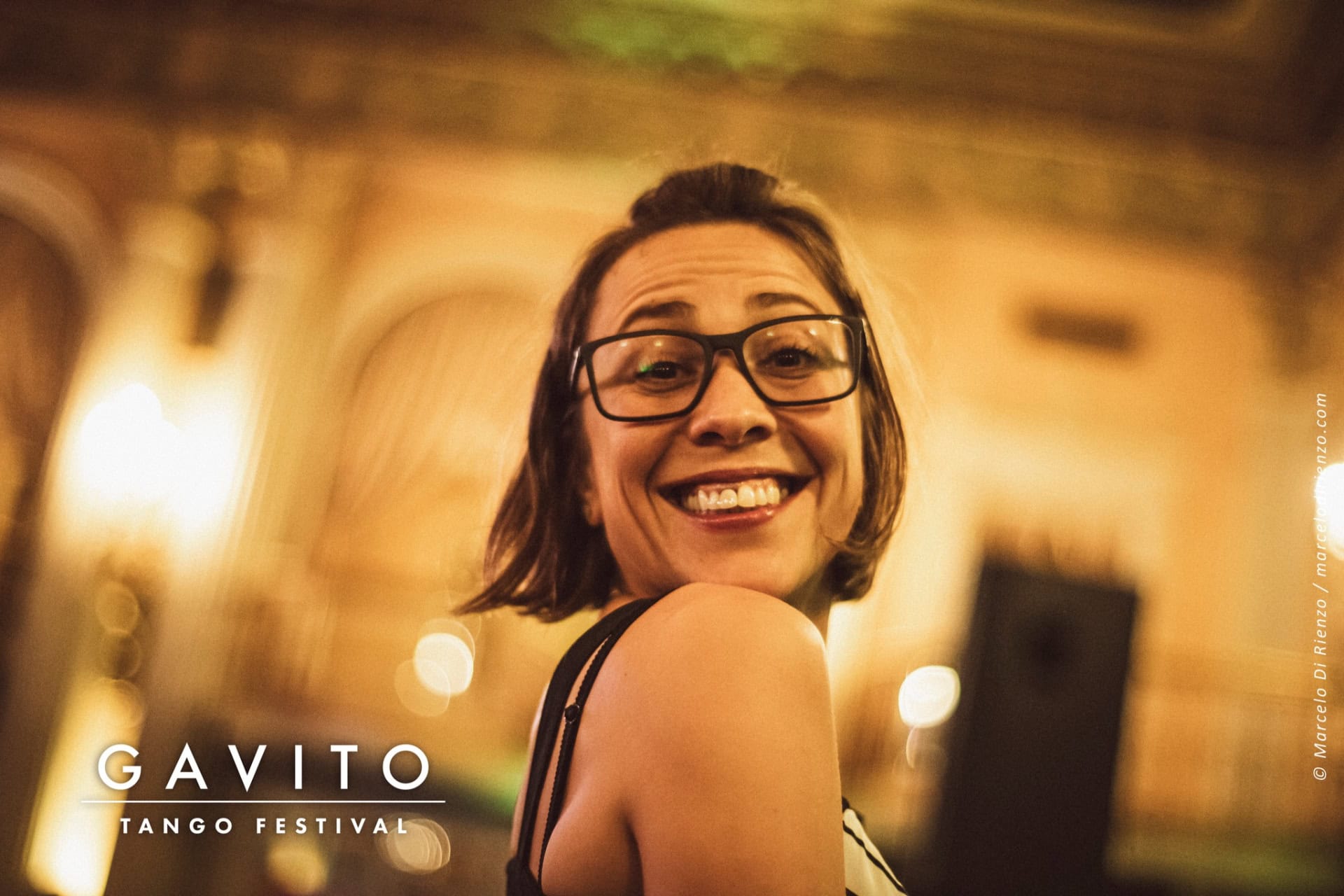A smiling woman with glasses poses in a warmly lit outdoor setting at night.