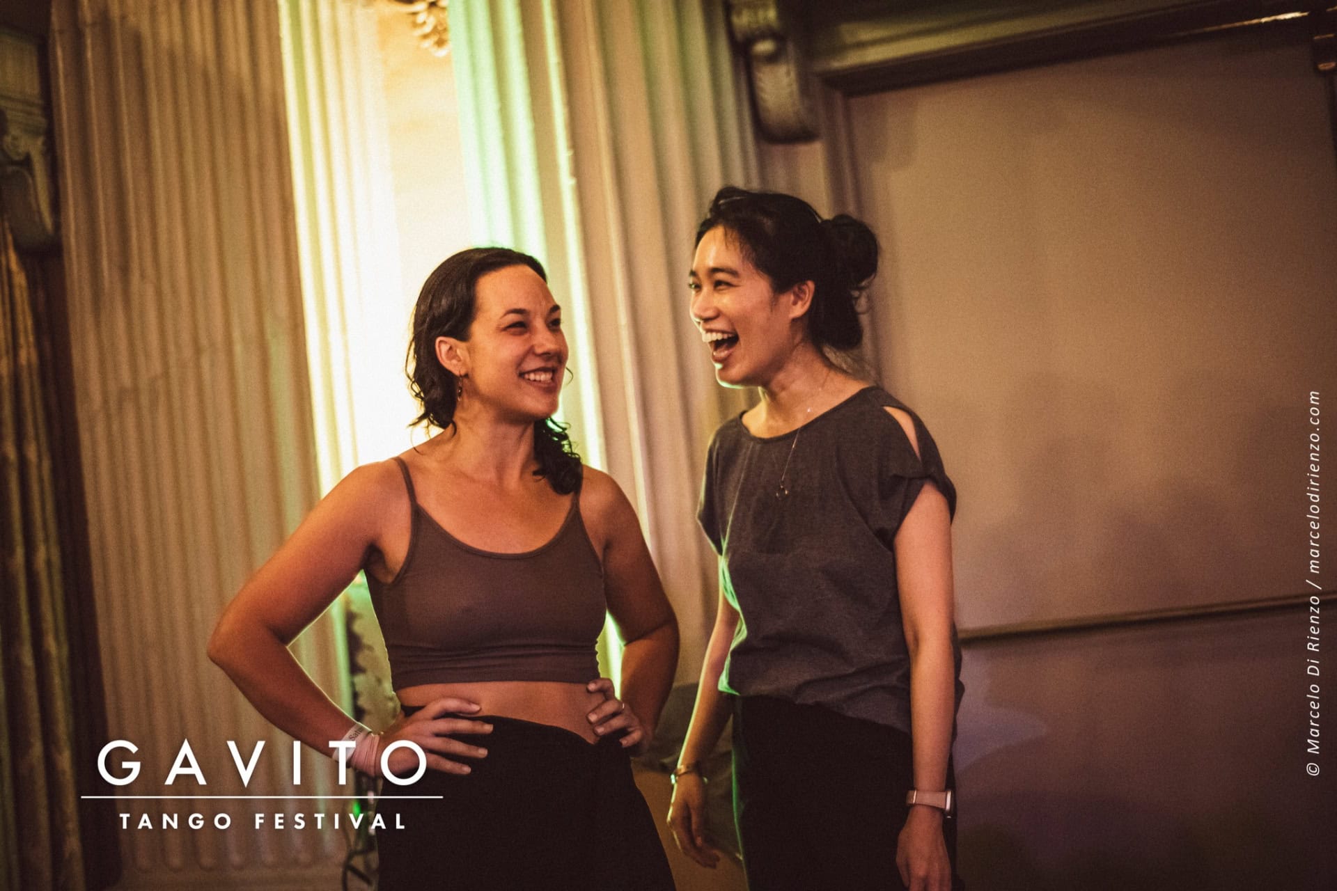 Two women in a warmly lit room smiling and talking.