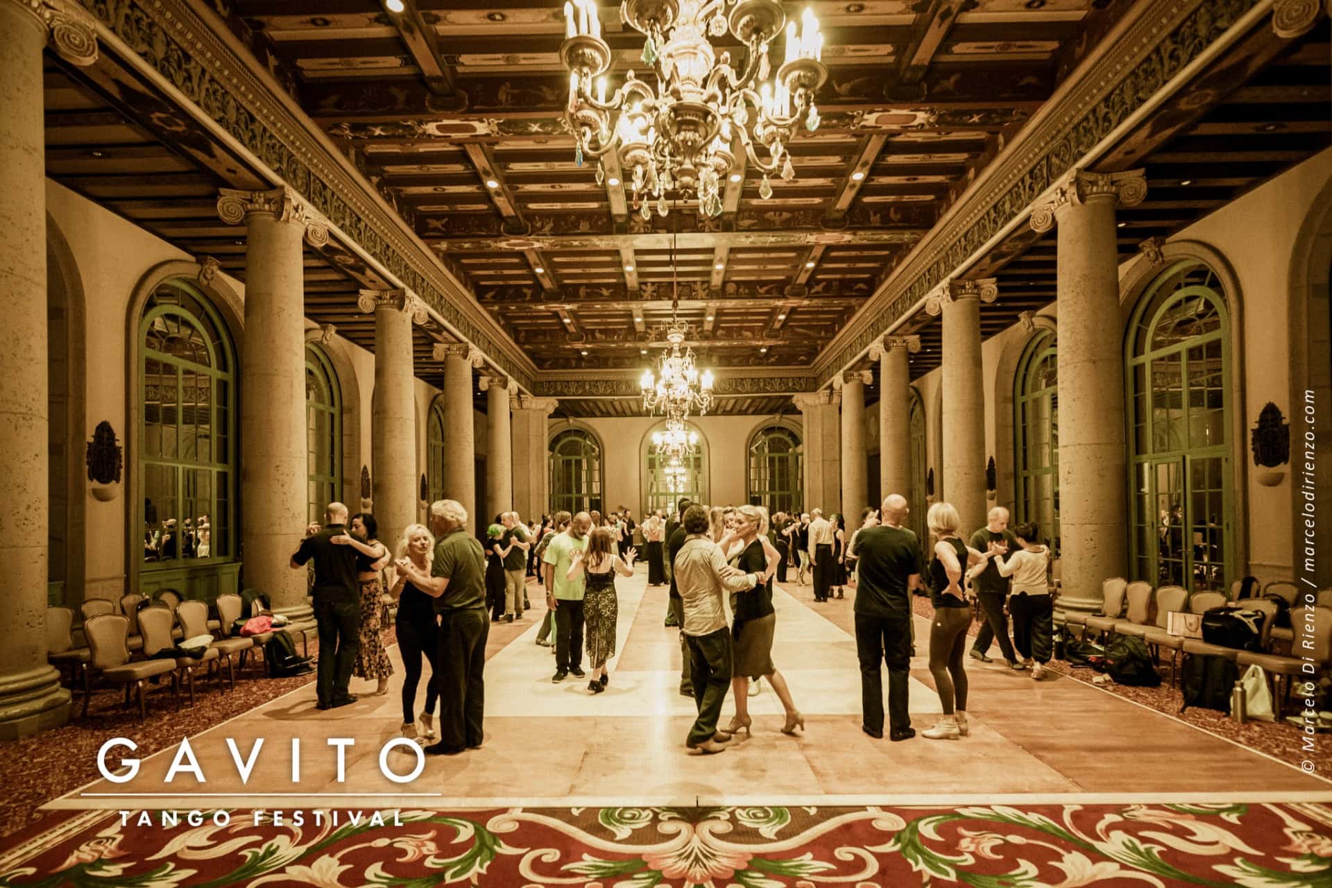 Elegant ballroom scene with guests dancing under ornate chandeliers.