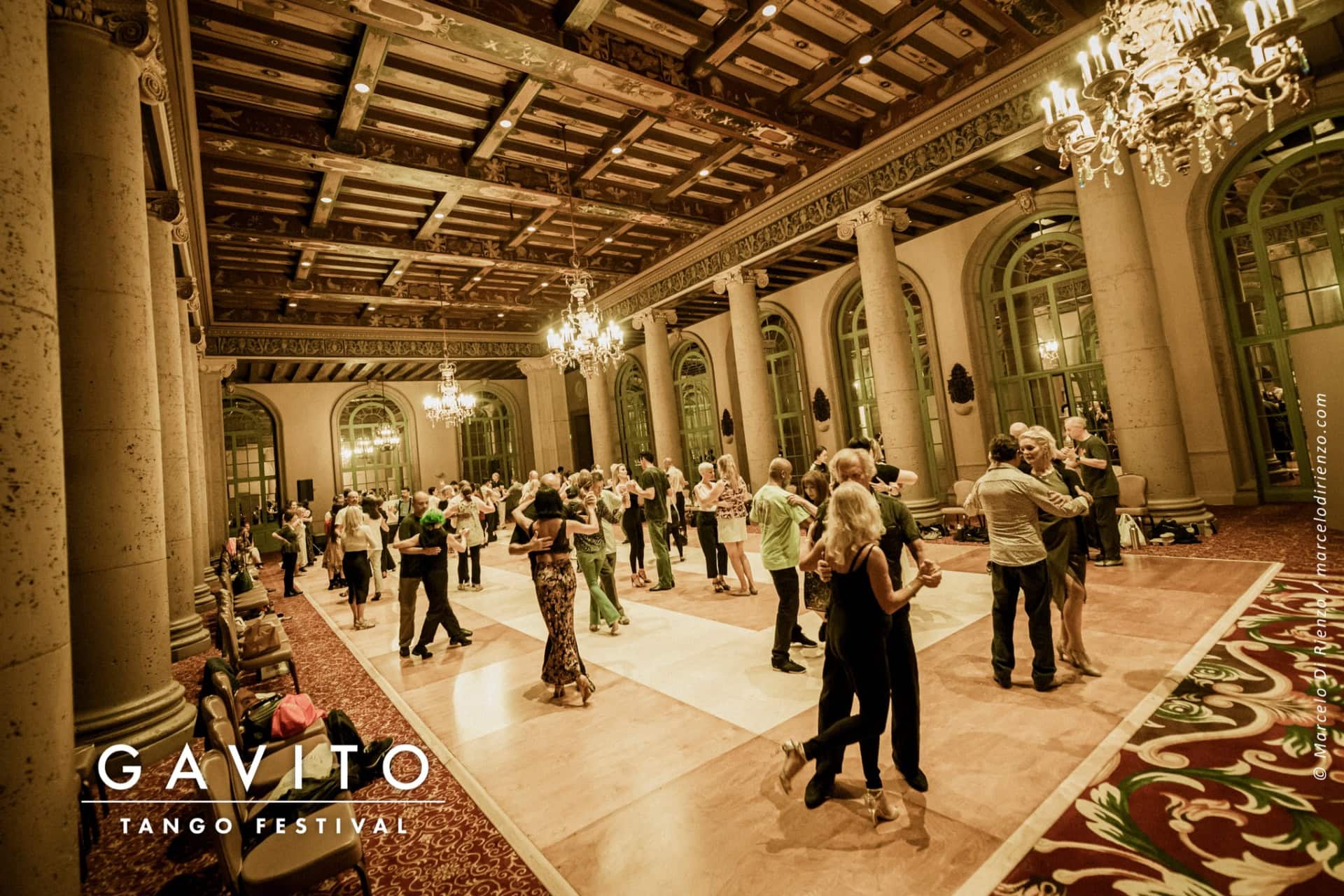 People dancing in an elegant, spacious ballroom with classical architecture.
