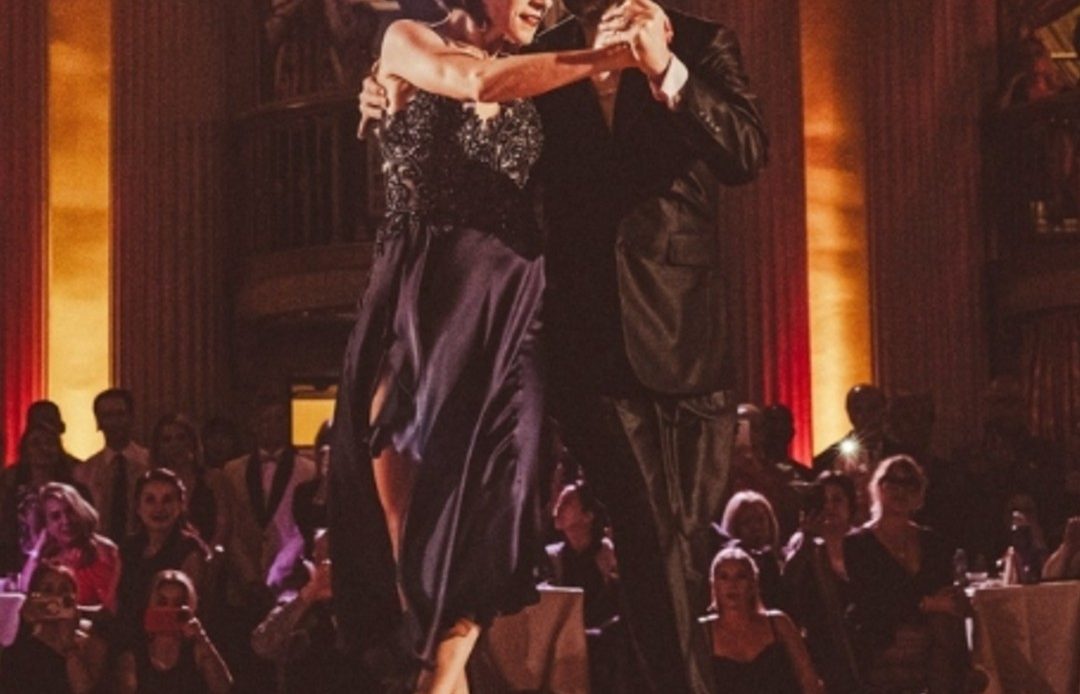 A dramatic dance duo performs a passionate tango on a dimly lit stage.