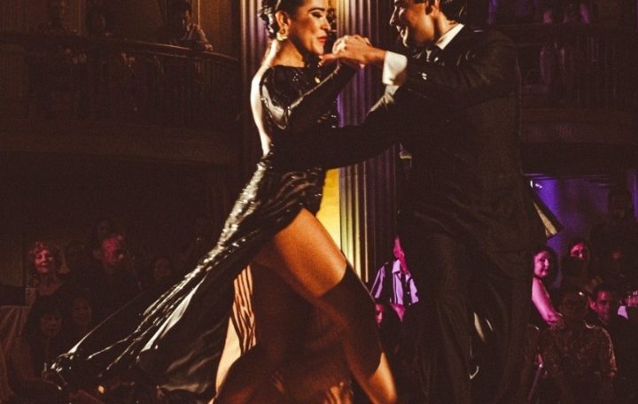 Couple passionately dancing tango on a dimly lit stage.