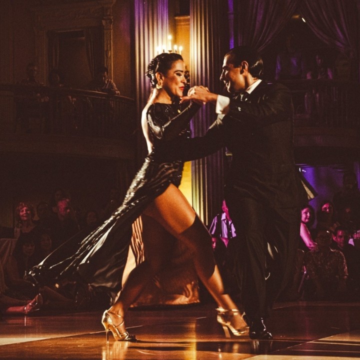 Couple passionately dancing tango on a dimly lit stage.