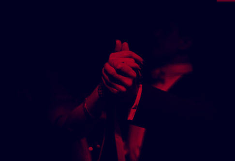 A person singing passionately into a microphone under red lighting.